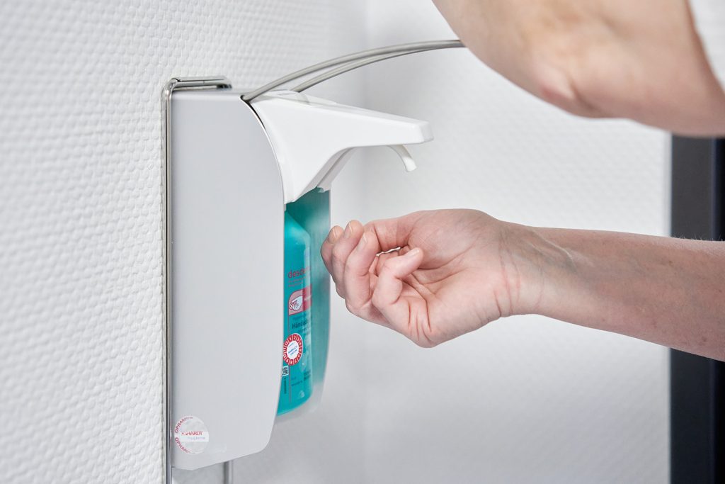 Hände bedienen einen Desinfektionsspender zur Händehygiene